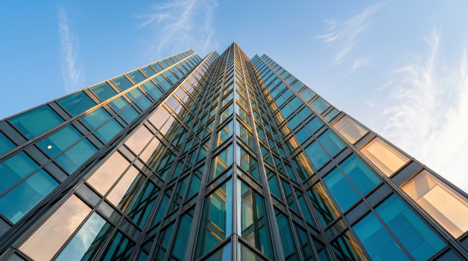 Glass and steel tower facade converging upward against clear blue sky with golden light on edges